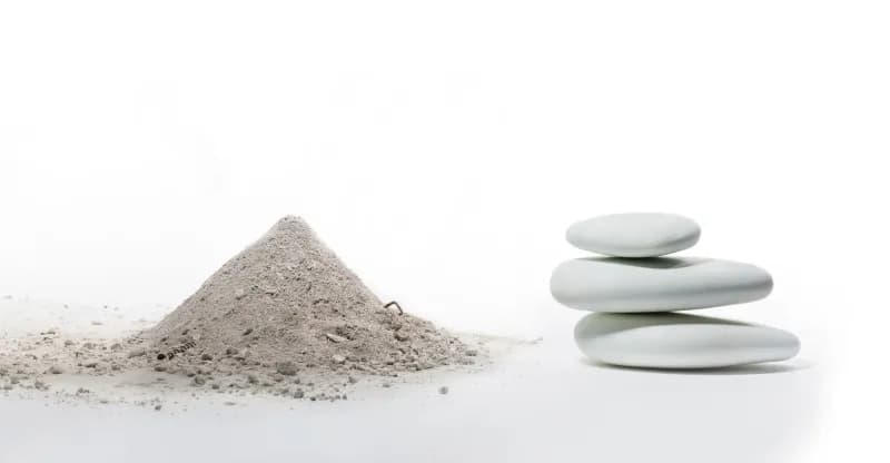 A pile of grey cremated pet ashes beside a stack of smooth, pale solidified remains stones on a white background.